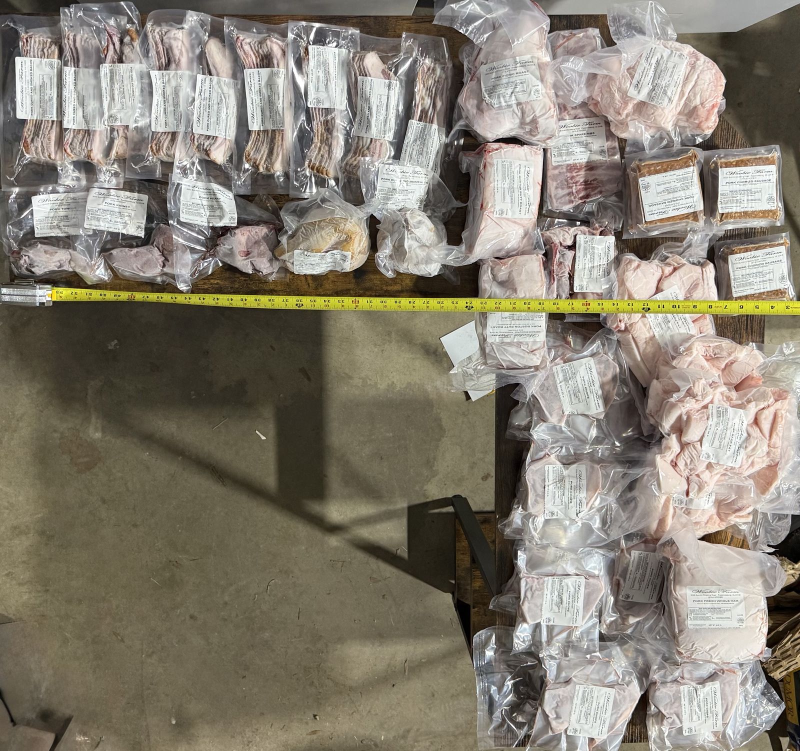 A half-hog share laid out on the table - vacuum-sealed roasts, chops, ground, and specialty cuts with a tape measure for scale